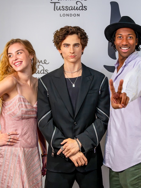 Wax figure of a celebrity at Madame Tussauds London with three visitors posing.