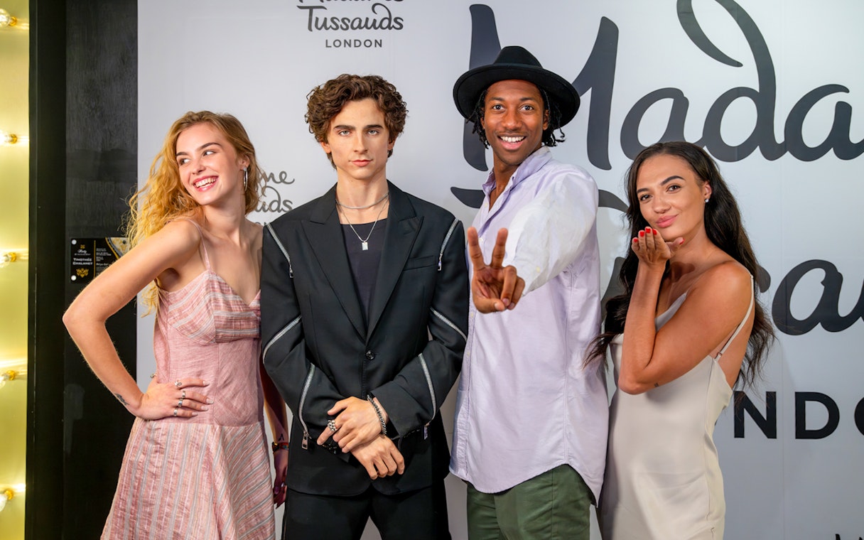 Wax figure of a celebrity at Madame Tussauds London with three visitors posing.