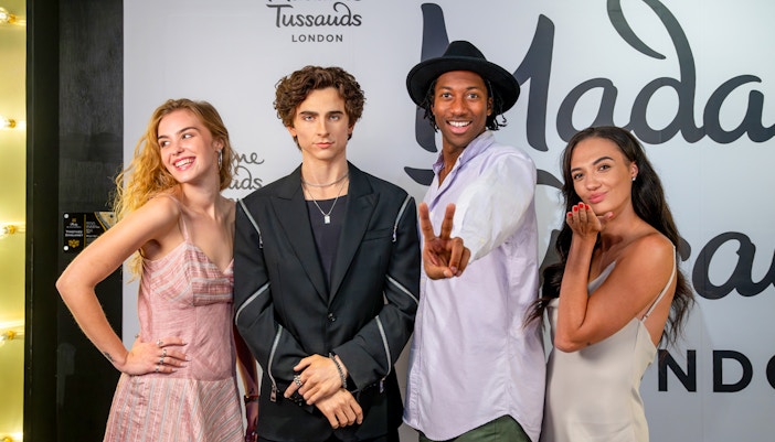 Wax figure of a celebrity at Madame Tussauds London with three visitors posing.