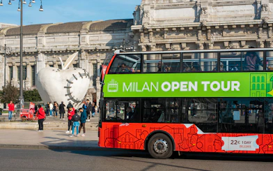 Milan hop-on hop-off tour bus near Central Station and apple sculpture.