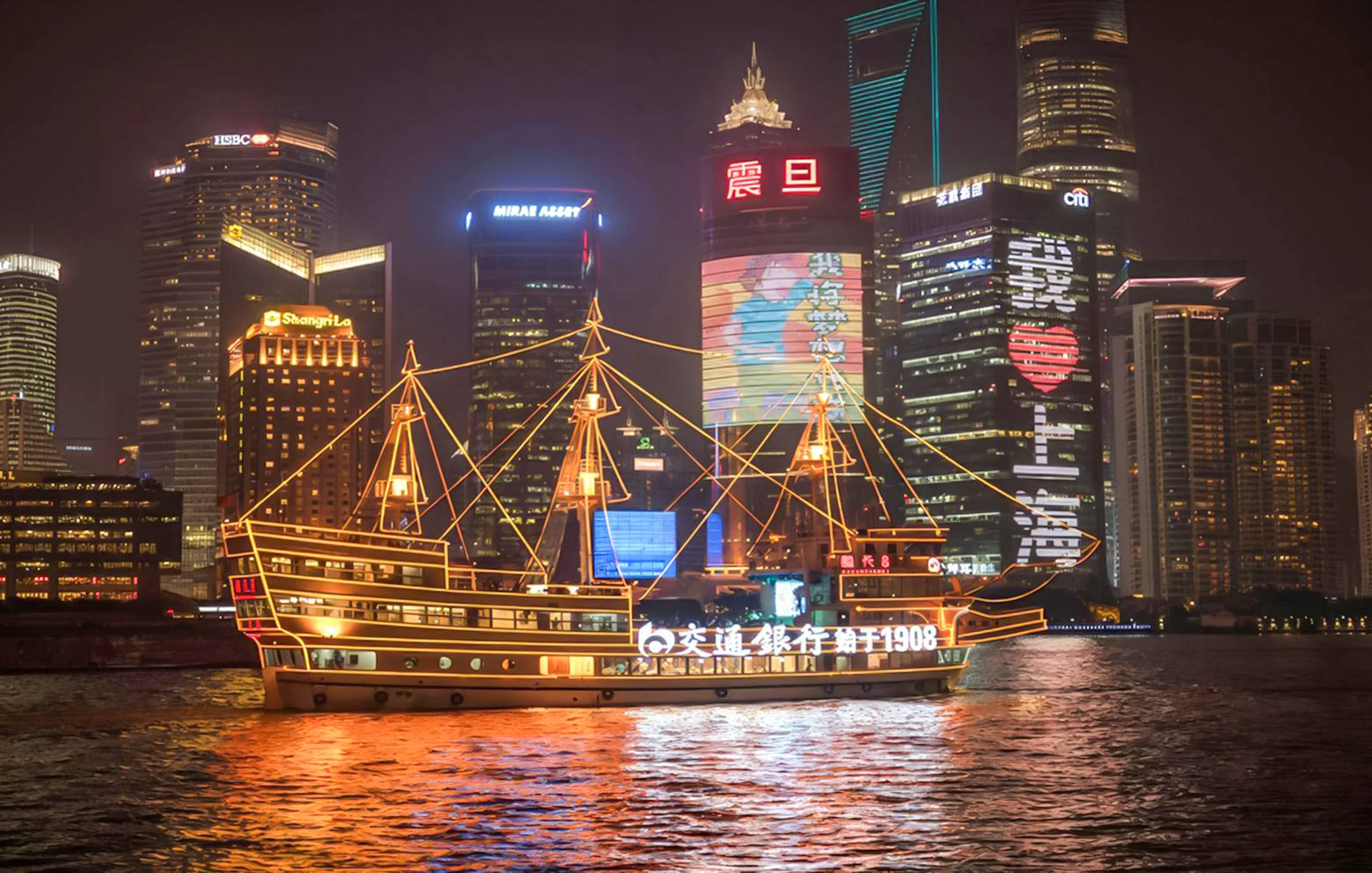 Cruise ship on Huangpu River with Shanghai's Bund and Lujiazui skyline at night.