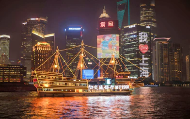 Cruise ship on Huangpu River with Shanghai's Bund and Lujiazui skyline at night.