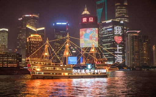 Cruise ship on Huangpu River with Shanghai's Bund and Lujiazui skyline at night.
