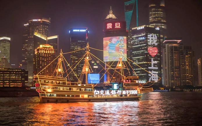 Cruise ship on Huangpu River with Shanghai's Bund and Lujiazui skyline at night.