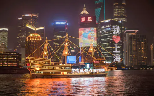 Cruise ship on Huangpu River with Shanghai's Bund and Lujiazui skyline at night.