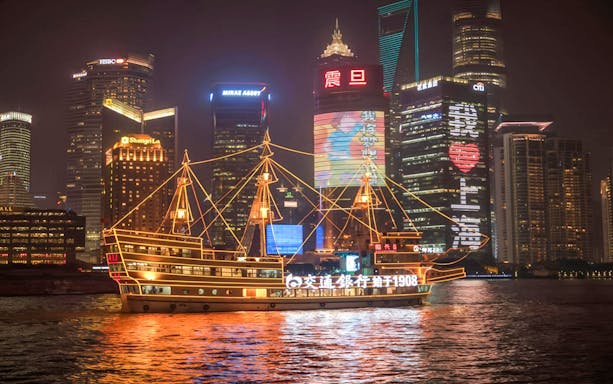 Cruise ship on Huangpu River with Shanghai's Bund and Lujiazui skyline at night.