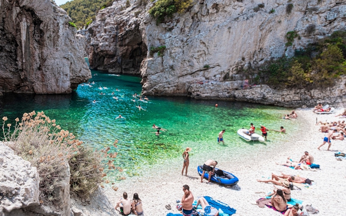 Stiniva beach in Croatia with swimmers in clear turquoise water surrounded by rocky cliffs.