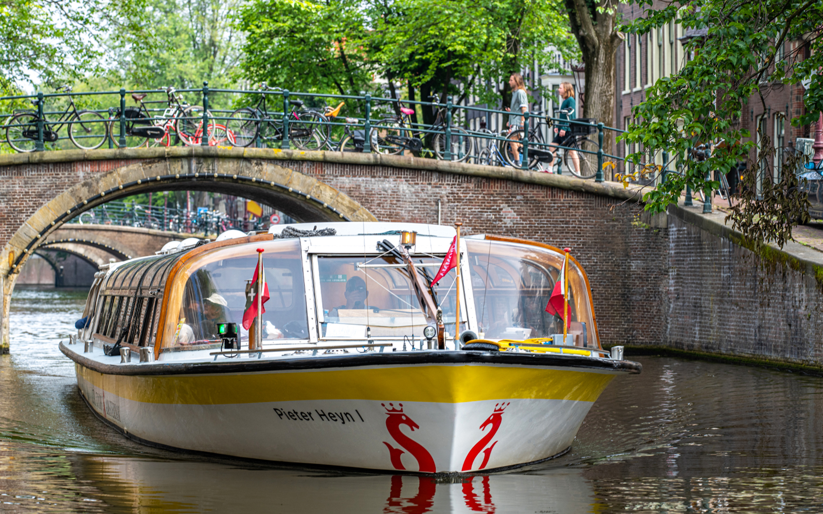 Canal boat cruising under a bridge in Amsterdam.
