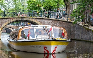 Canal boat cruising under a bridge in Amsterdam.