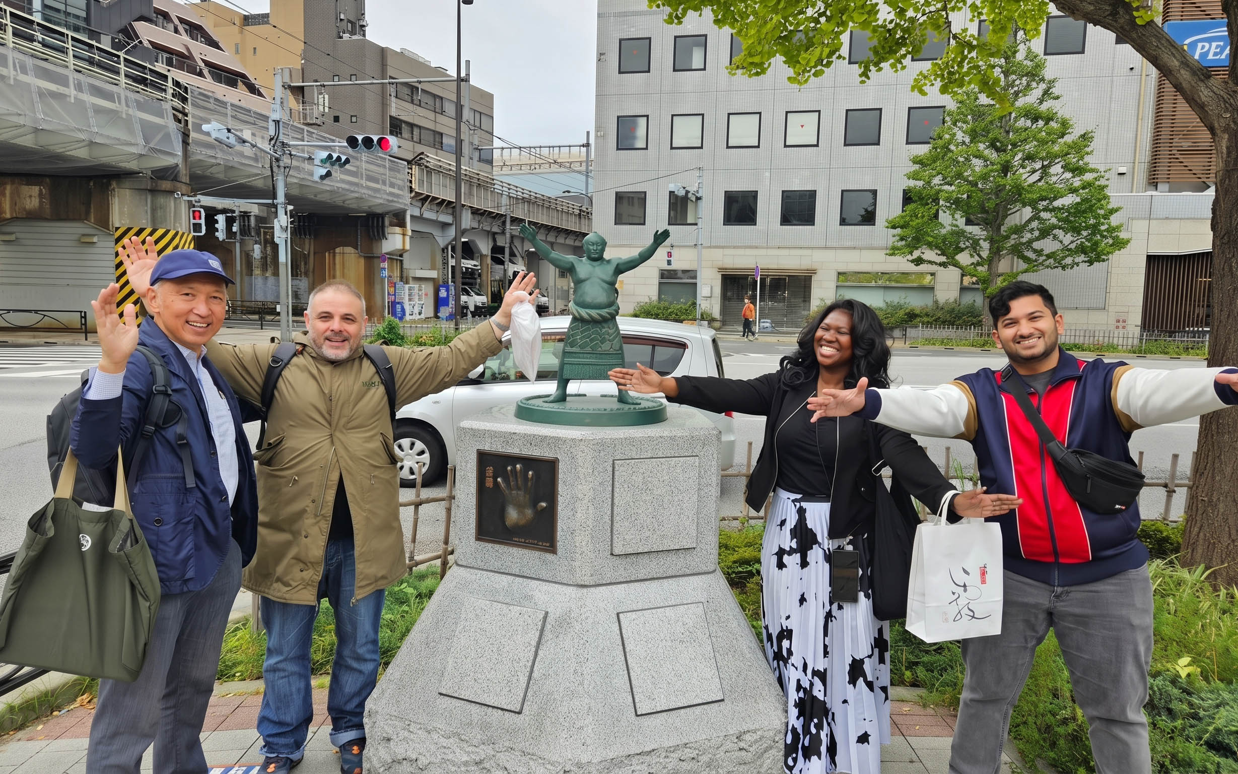 Visitors posing with a sumo wrestler statue in Tokyo, Japan, near the Grand Sumo Tournament venue.
