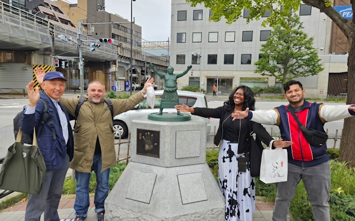 Visitors posing with a sumo wrestler statue in Tokyo, Japan, near the Grand Sumo Tournament venue.