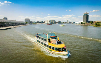 Dutch Pancake cruise boat on Amsterdam's IJ River with cityscape in background.