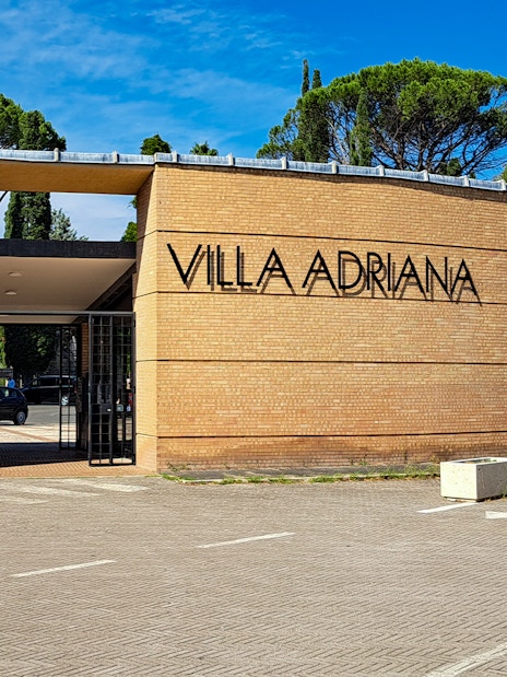 Entrance to Villa Adriana in Tivoli, Italy, with trees and clear sky in the background.