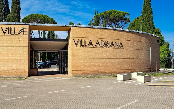 Entrance to Villa Adriana in Tivoli, Italy, with trees and clear sky in the background.