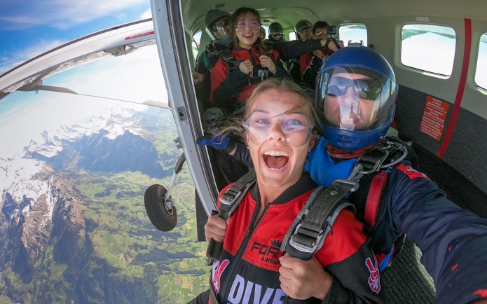 Tourists preparing to skydive from a plane over scenic mountains.