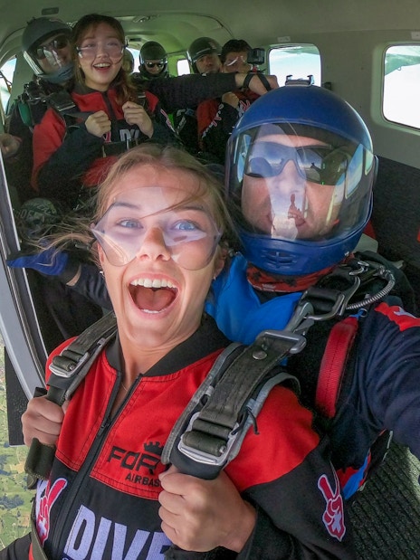 Tourists preparing to skydive from a plane over scenic mountains.