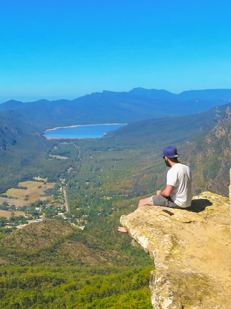 Person sitting on a rock ledge overlooking Grampians National Park landscape, Melbourne day tour.