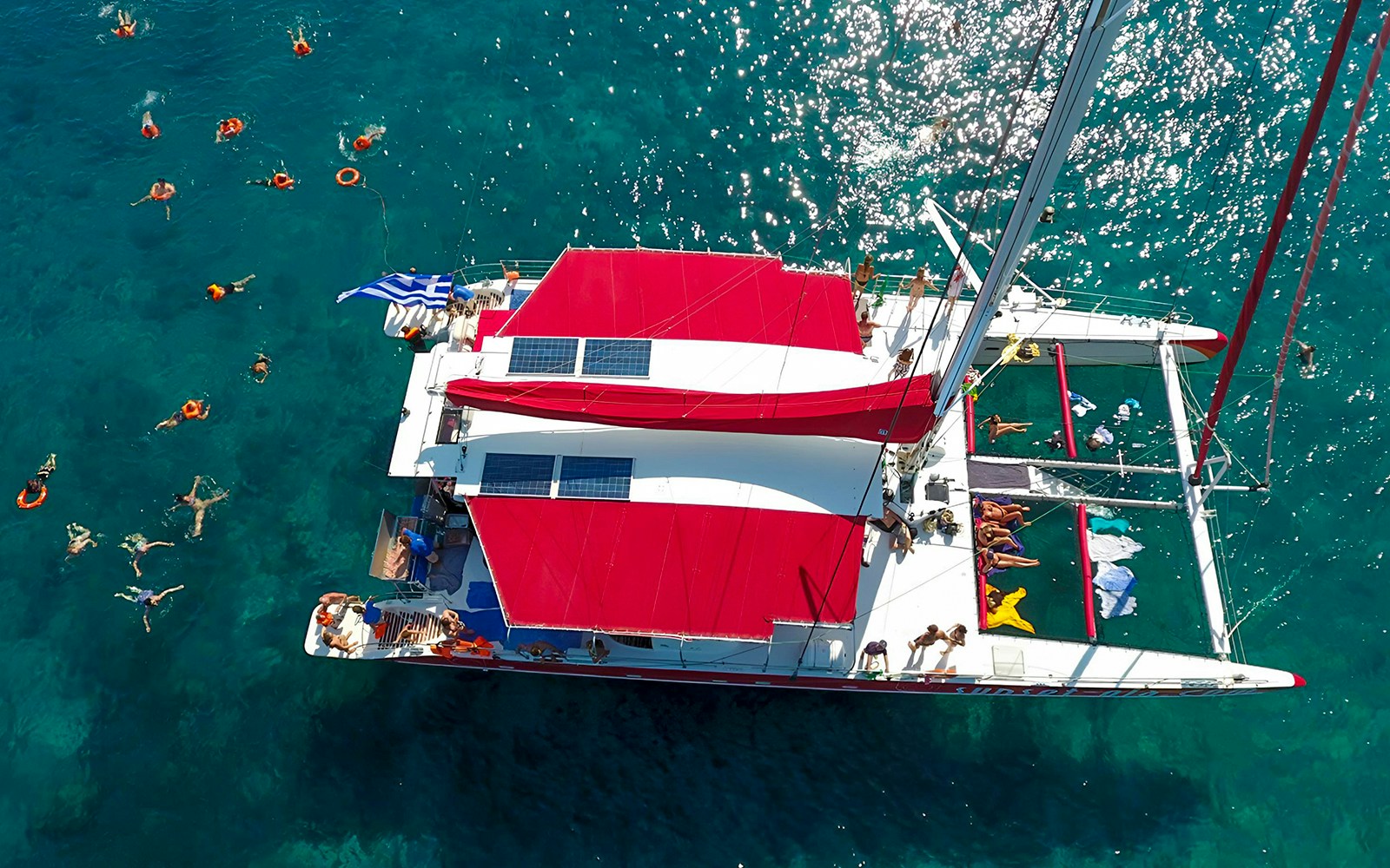 Catamaran sailing near Santorini's coastline with passengers enjoying BBQ and open bar.