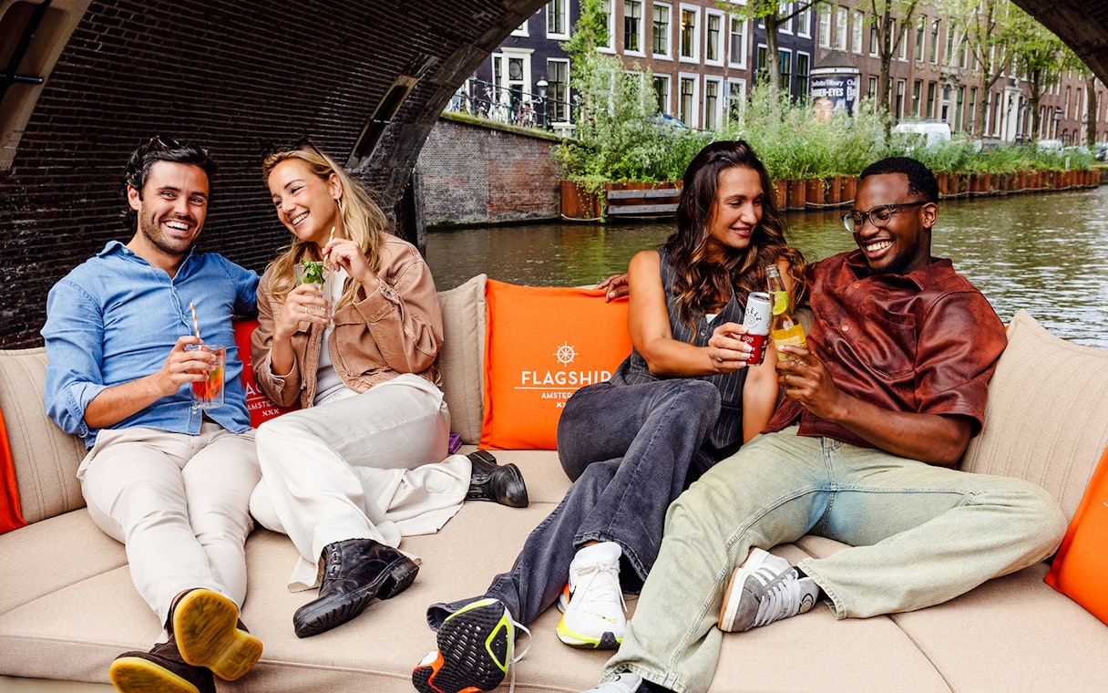 Guests enjoying drinks on a luxury open boat cruise in Amsterdam canal.