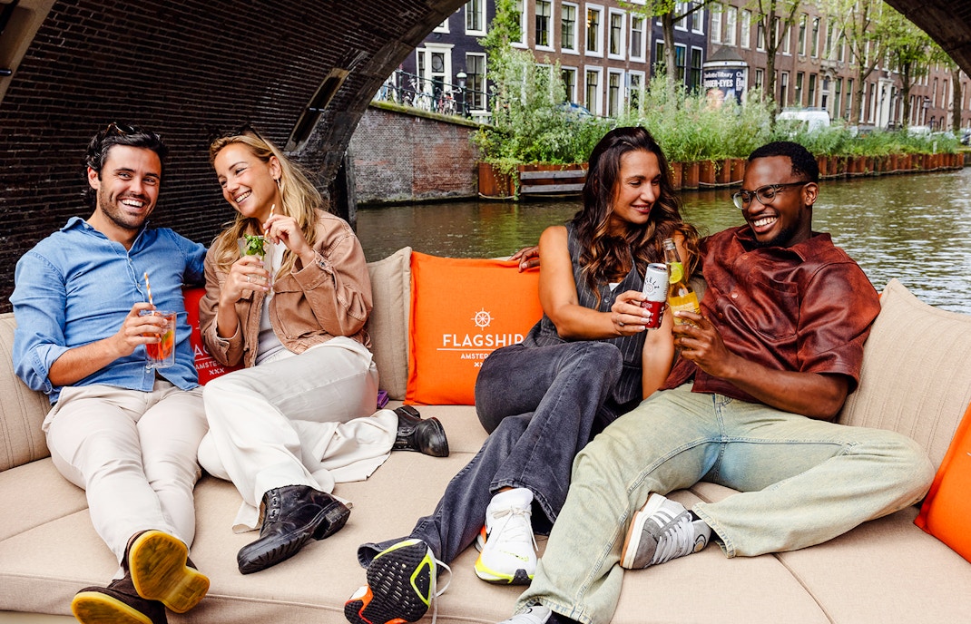 Guests enjoying drinks on a luxury open boat cruise in Amsterdam canal.