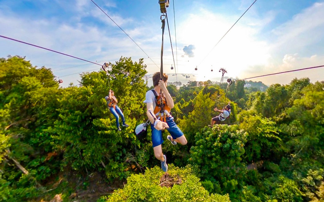 Visitors ziplining over lush greenery at Mega Adventure Park, Singapore.