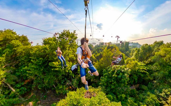 Visitors ziplining over lush greenery at Mega Adventure Park, Singapore.