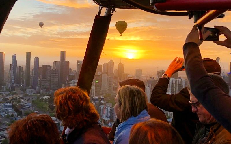 Hot air balloon passengers view sunrise over Melbourne skyline.