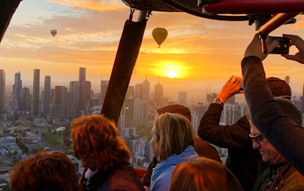 Hot air balloon passengers view sunrise over Melbourne skyline.