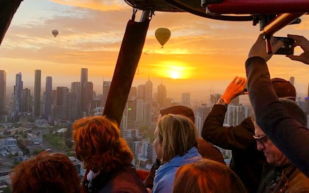 Hot air balloon passengers view sunrise over Melbourne skyline.