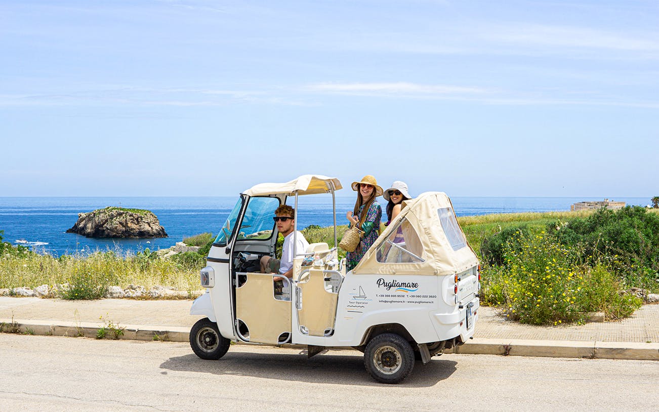 Tuk-tuk with tourists on coastal road in Polignano a Mare, Italy.