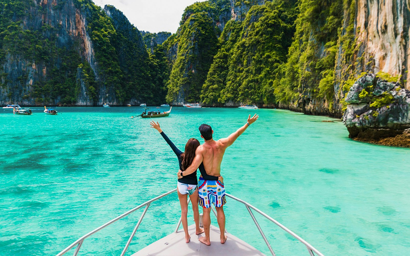 Couple on boat exploring Pileh Lagoon surrounded by cliffs and turquoise water.