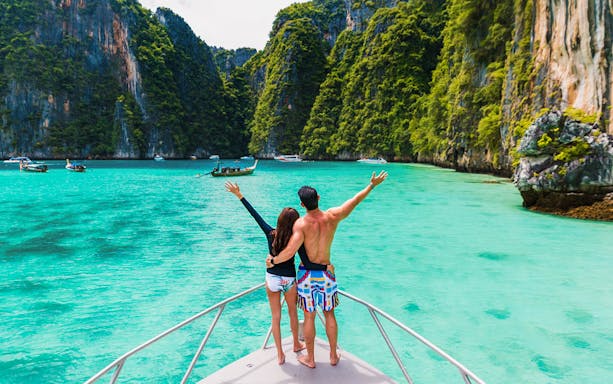 Couple on boat exploring Pileh Lagoon surrounded by cliffs and turquoise water.
