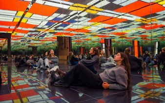Visitors seated in a mirrored room with colorful ceiling at Dutch Masters Exhibition, Fabrique des Lumières.