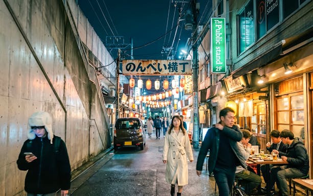 Woman walking through Shibuya street with food stalls and lanterns in Tokyo.
