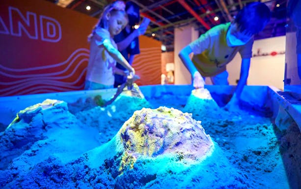 Children engaging in a hands-on sand activity at Chaos Lab.