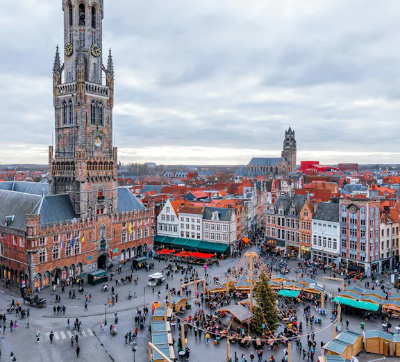 Cityscape of Bruges main square with Belfry Tower and market stalls.