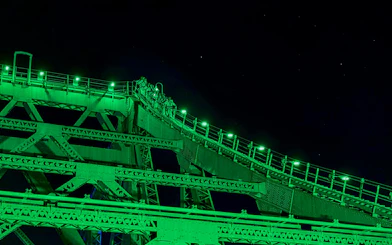 Climbers ascending Story Bridge at night, illuminated by green lights in Brisbane.