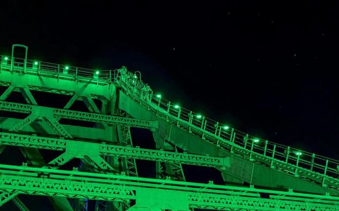 Climbers ascending Story Bridge at night, illuminated by green lights in Brisbane.