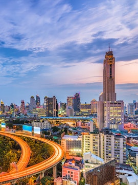 Baiyoke Sky Hotel towering over Bangkok cityscape at dusk with illuminated highway.