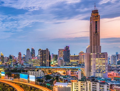 Baiyoke Sky Hotel towering over Bangkok cityscape at dusk with illuminated highway.