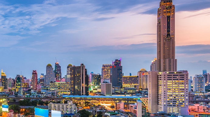 Baiyoke Sky Hotel towering over Bangkok cityscape at dusk with illuminated highway.
