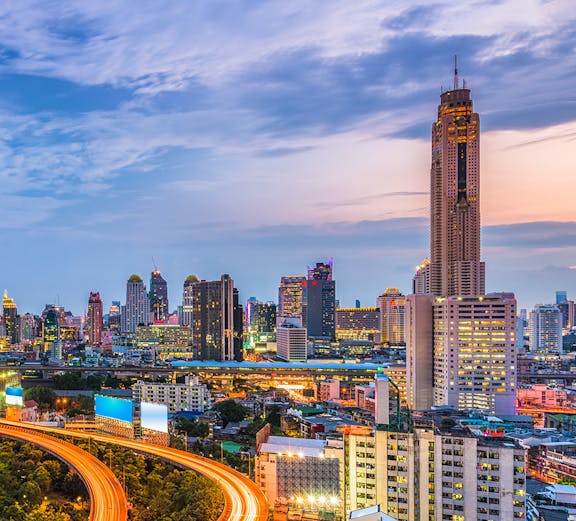 Baiyoke Sky Hotel towering over Bangkok cityscape at dusk with illuminated highway.