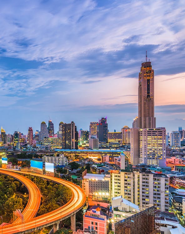 Baiyoke Sky Hotel towering over Bangkok cityscape at dusk with illuminated highway.