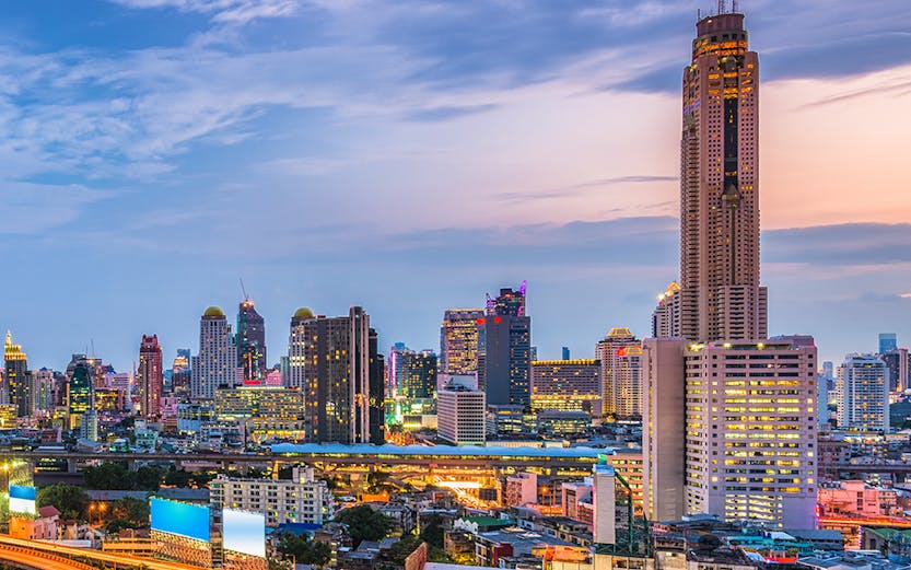Baiyoke Sky Hotel towering over Bangkok cityscape at dusk with illuminated highway.