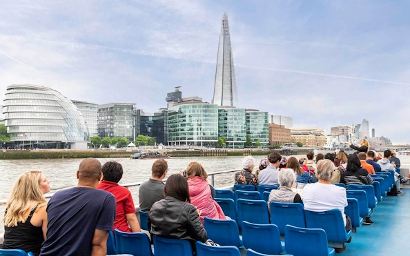 People on a Thames River cruise with views of The Shard and City Hall in London.
