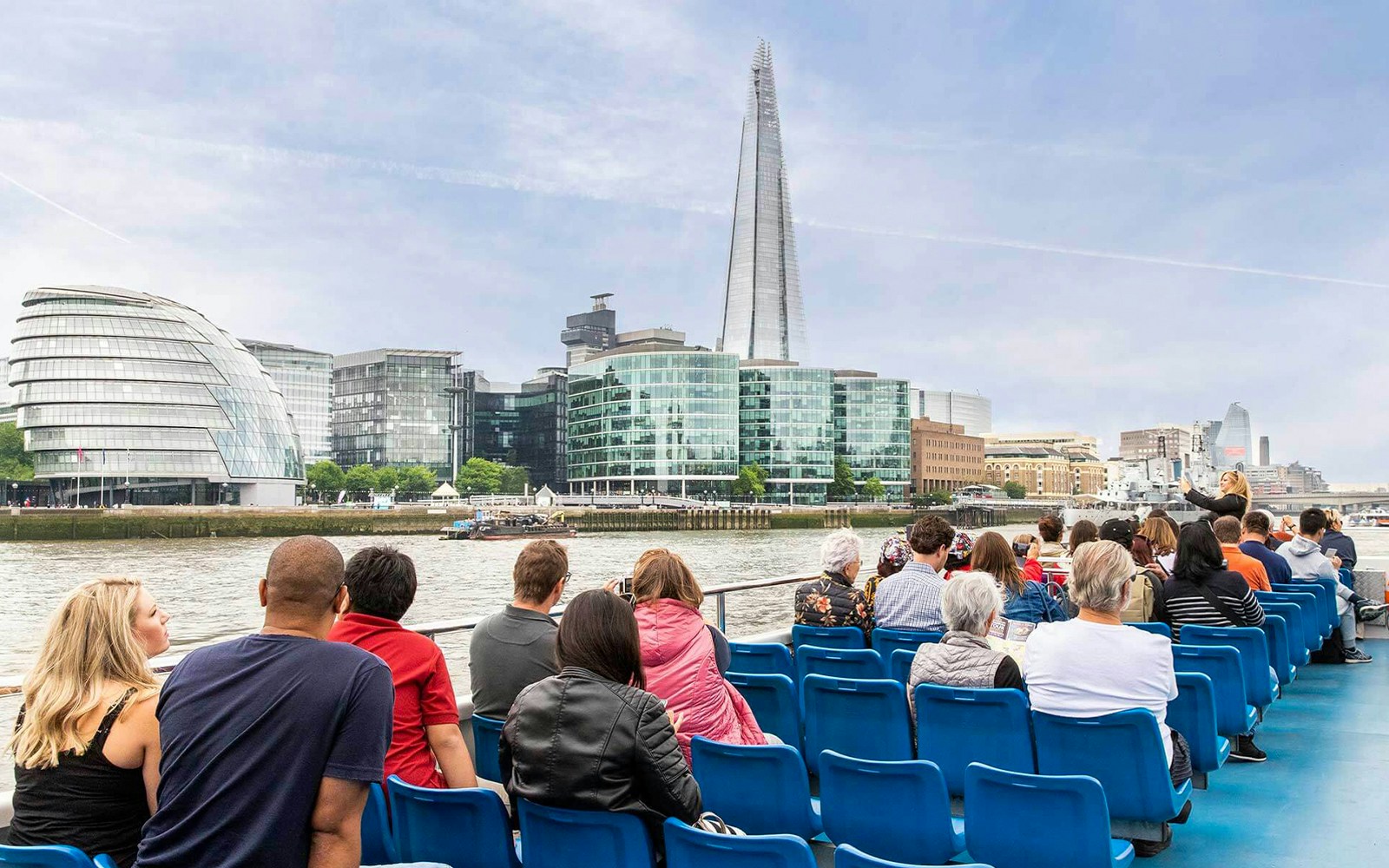 People on a Thames River cruise with views of The Shard and City Hall in London.