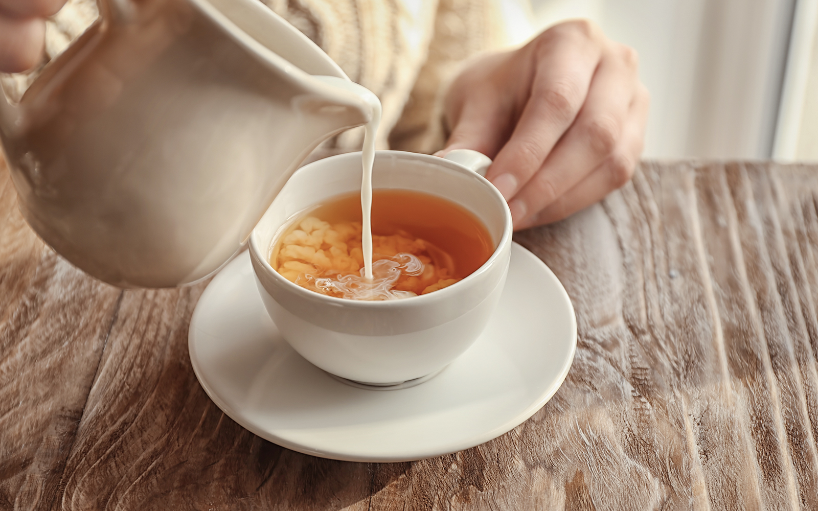 Milk being poured into a cup of chai on a wooden table.