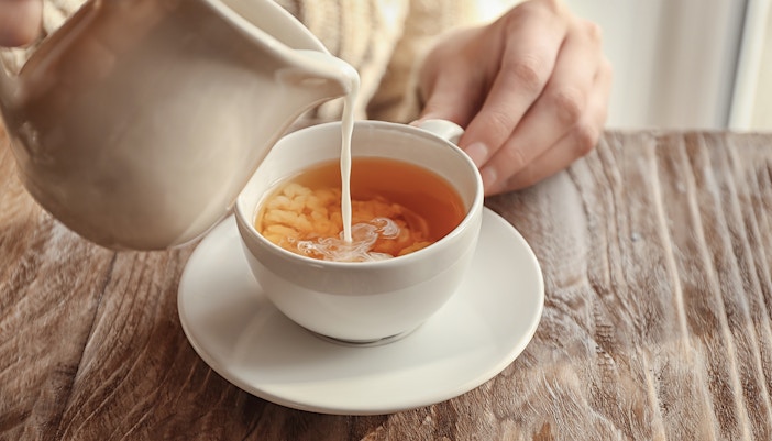 Milk being poured into a cup of chai on a wooden table.