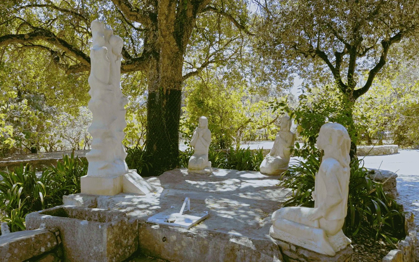 Stone sculptures of religious figures under trees in Fatima, Portugal.