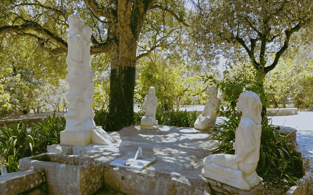 Stone sculptures of religious figures under trees in Fatima, Portugal.
